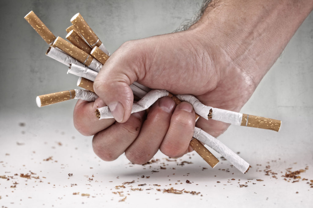 Mão amassando cigarros simbolizando o ato de parar de fumar