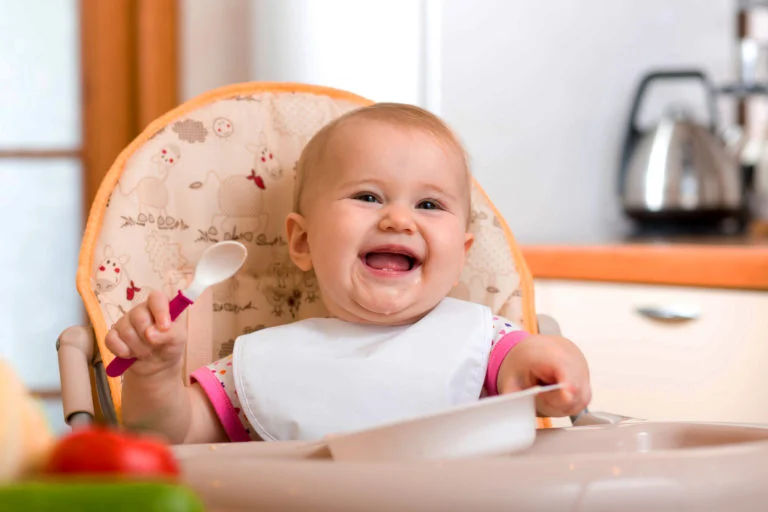 Bebê sorrindo com prato e colher na mão