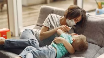 Mãe usando máscara e dando remédio para o seu filho.