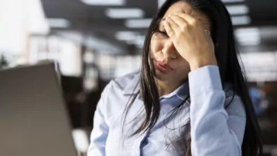 rosto de mulher morena com as mãos na testa em ambiente de trabalho demostrando cansaço