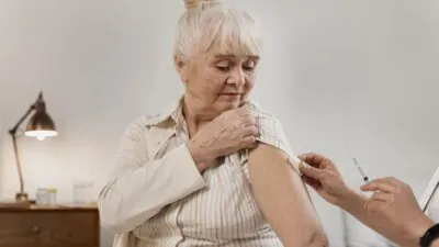 Mãos de enfermeiro preparando braço para vacina em uma mulher idosa