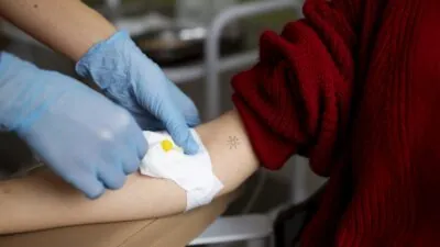 Braço é manipulada para doação de sangue por mãos com luvas.